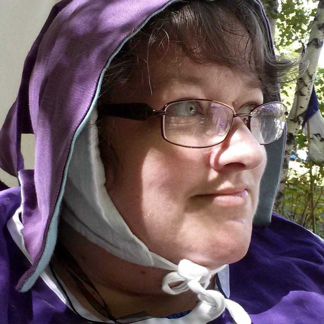Our 2024 guest of honor HollyAnn. She is wearing historical garments of purple and white and wearing oval glasses. 